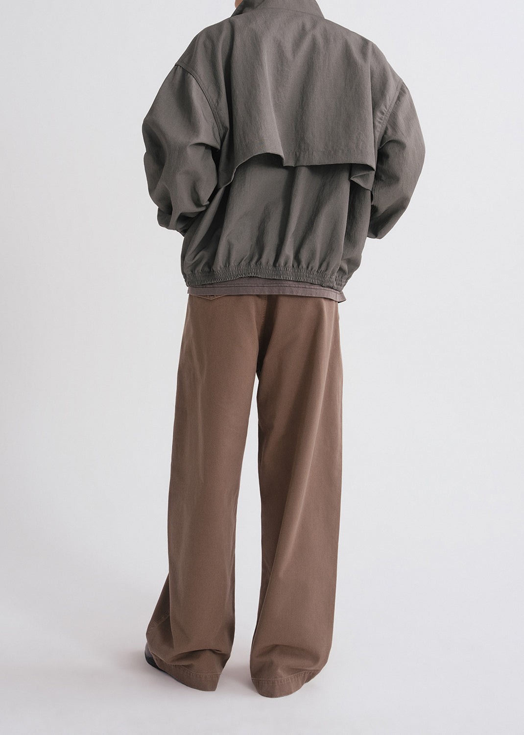 Person wearing green jacket over brown shirt and brown pants on a grey background