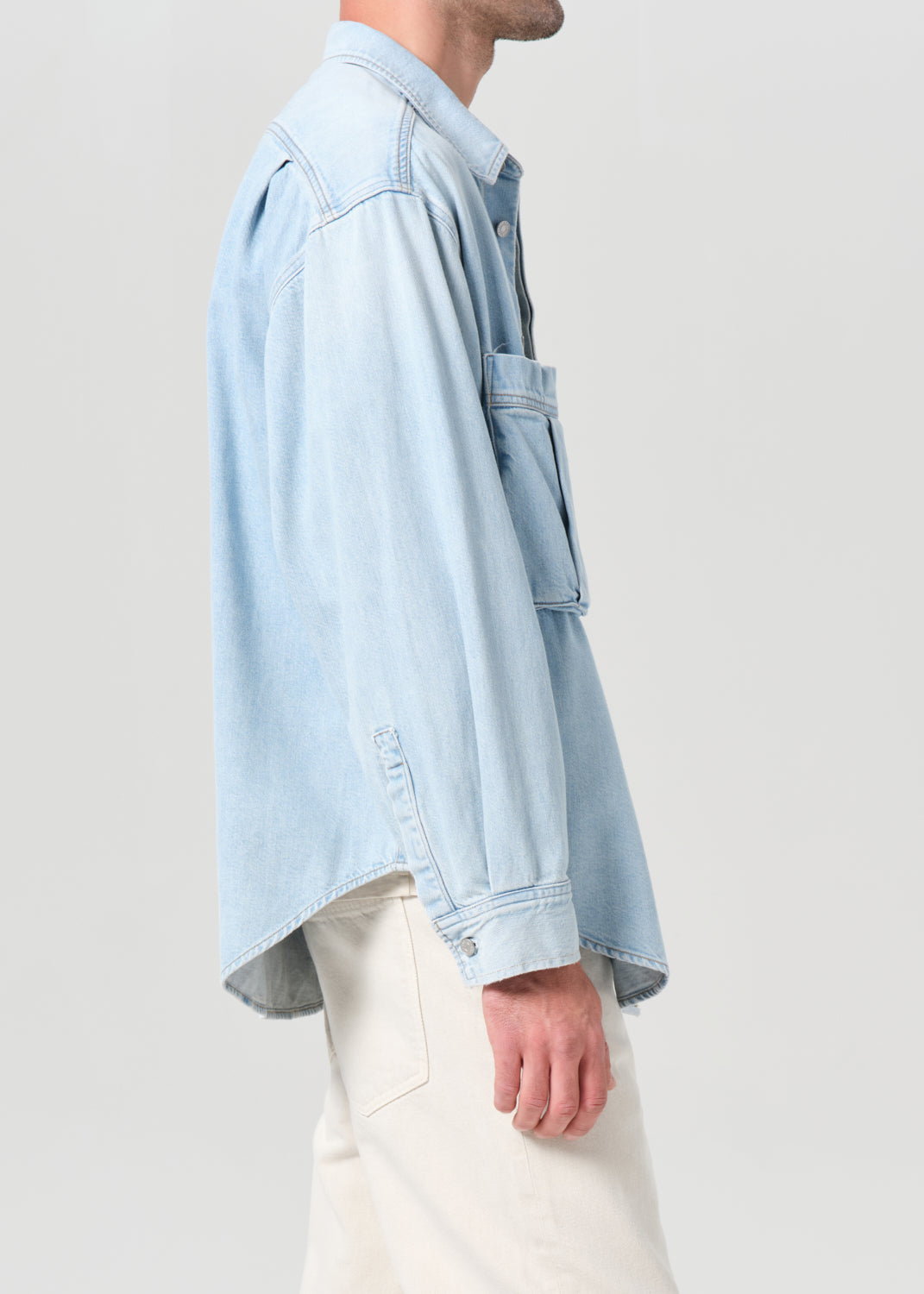 Person wearing a light blue denim shirt and white pants on a plain background