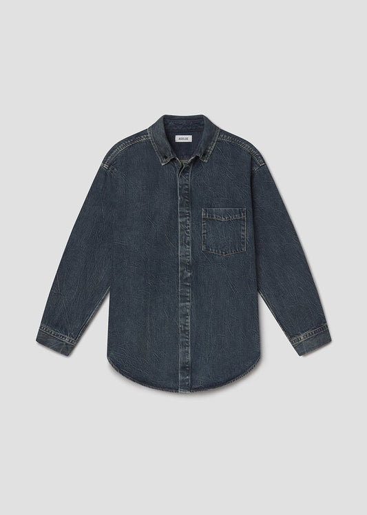 A dark blue denim long-sleeve button-up shirt with a chest pocket, laid flat against a grey background.
