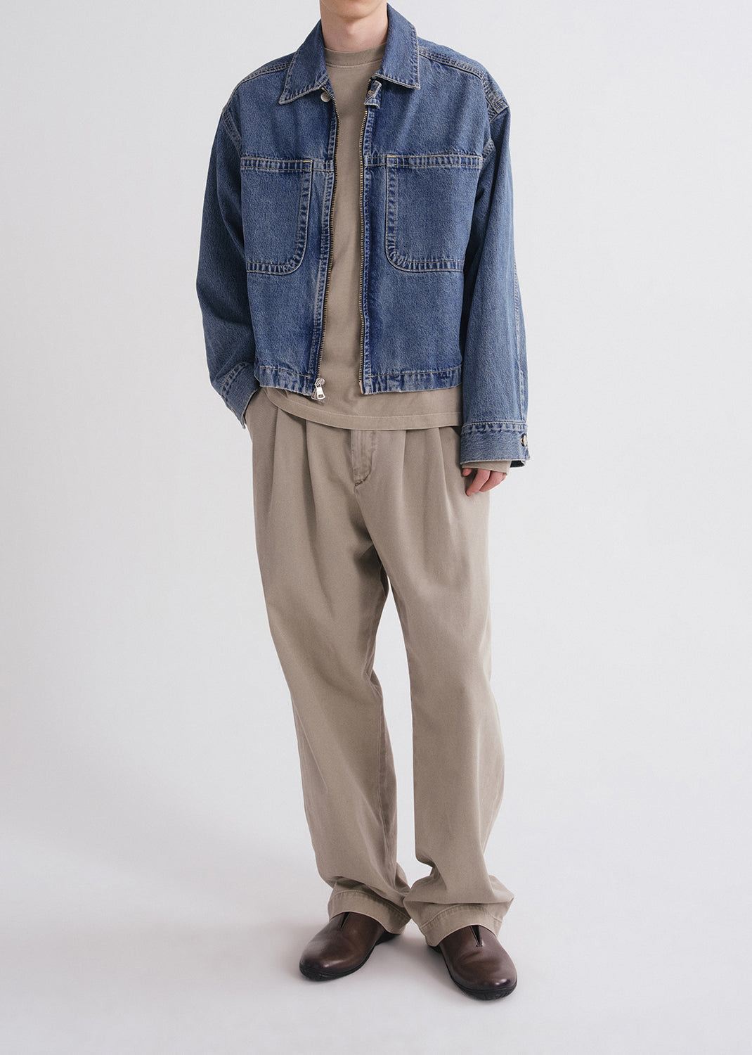 Person wearing a denim jacket, beige shirt, and pants on a grey background
