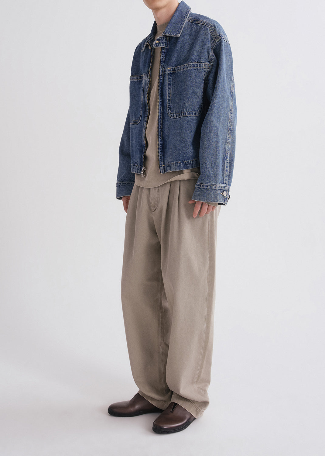 Person wearing a denim jacket, beige pants, and brown shoes on a grey background
