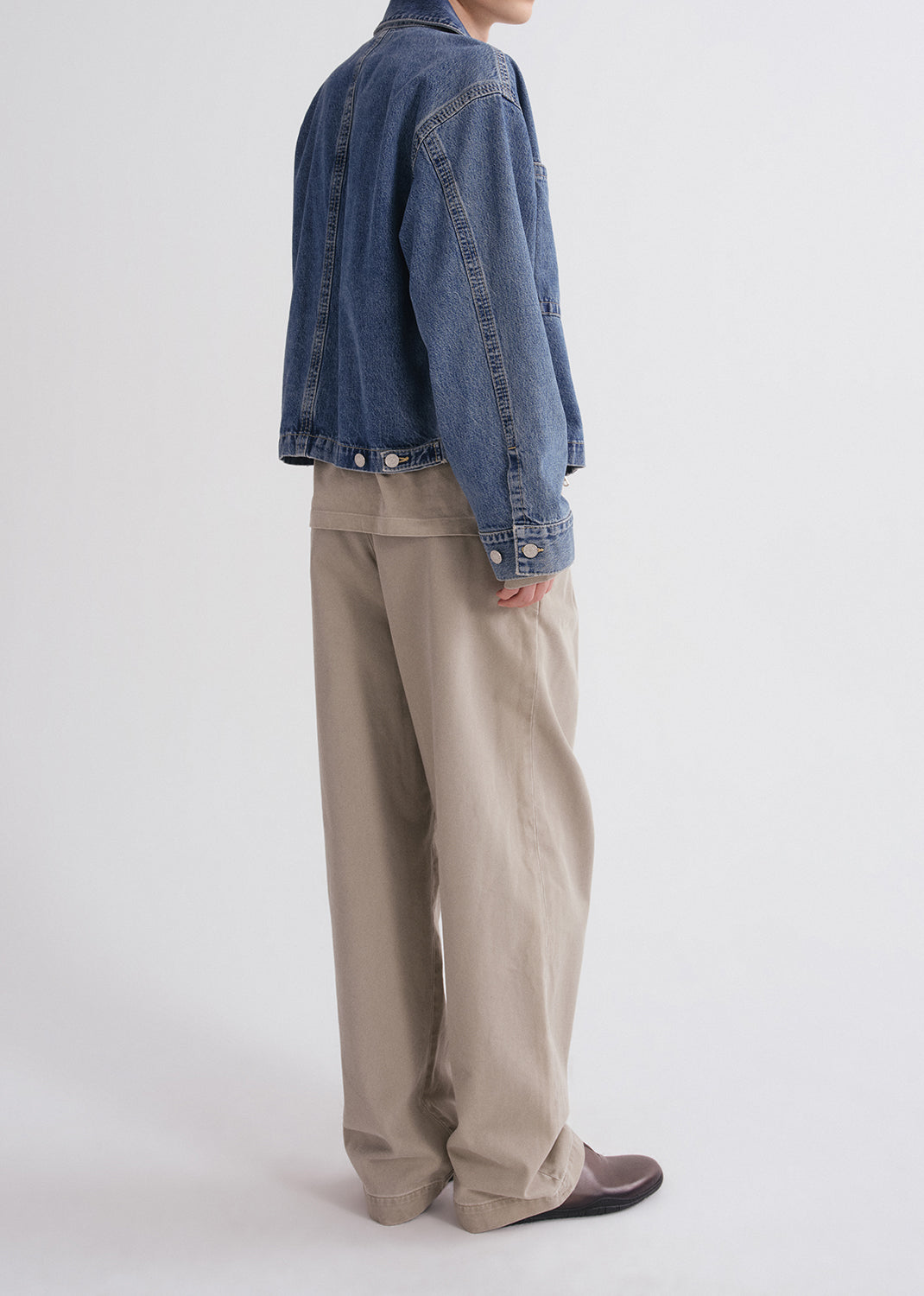 Person wearing a blue denim jacket and beige pants on a grey background