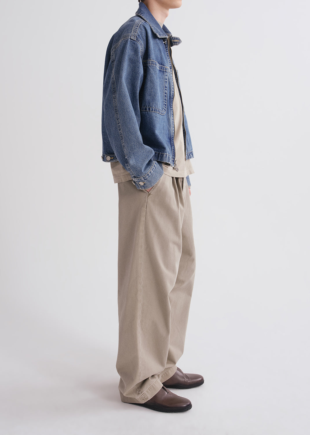 Person wearing a denim jacket and beige pants on a grey background