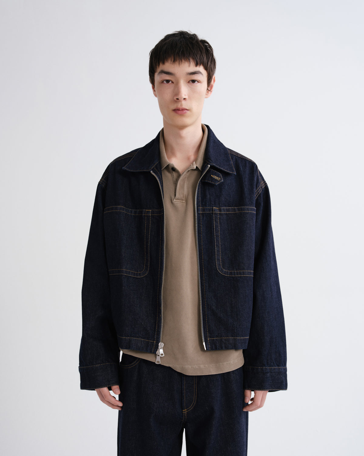 Man wearing a dark denim jacket over a beige shirt on a white background