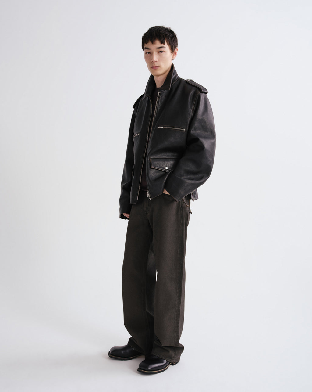 Person wearing a black leather jacket and pants on a grey background
