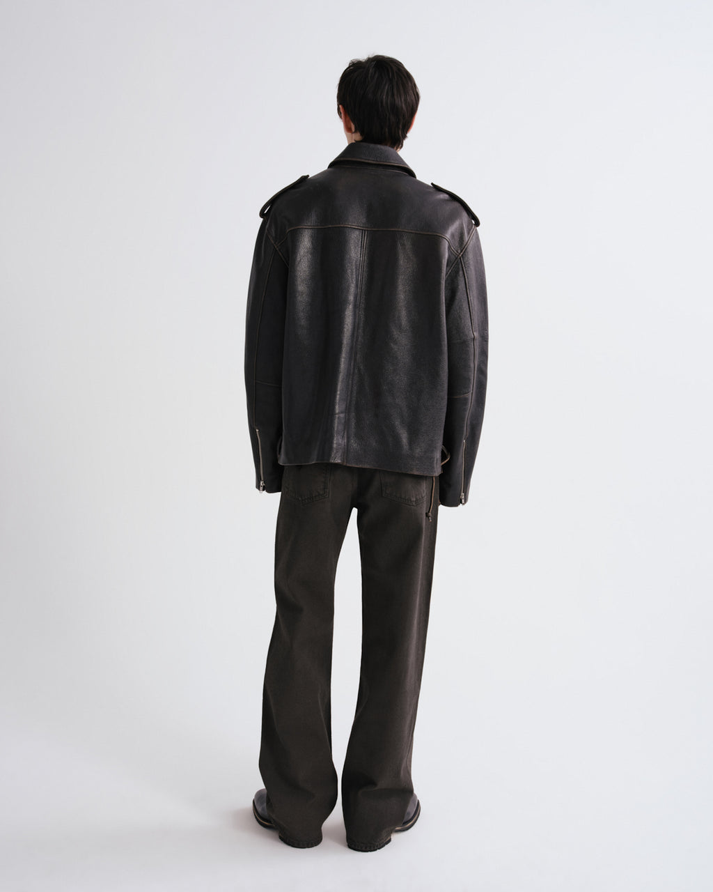 Person wearing a black leather jacket and pants on a grey background