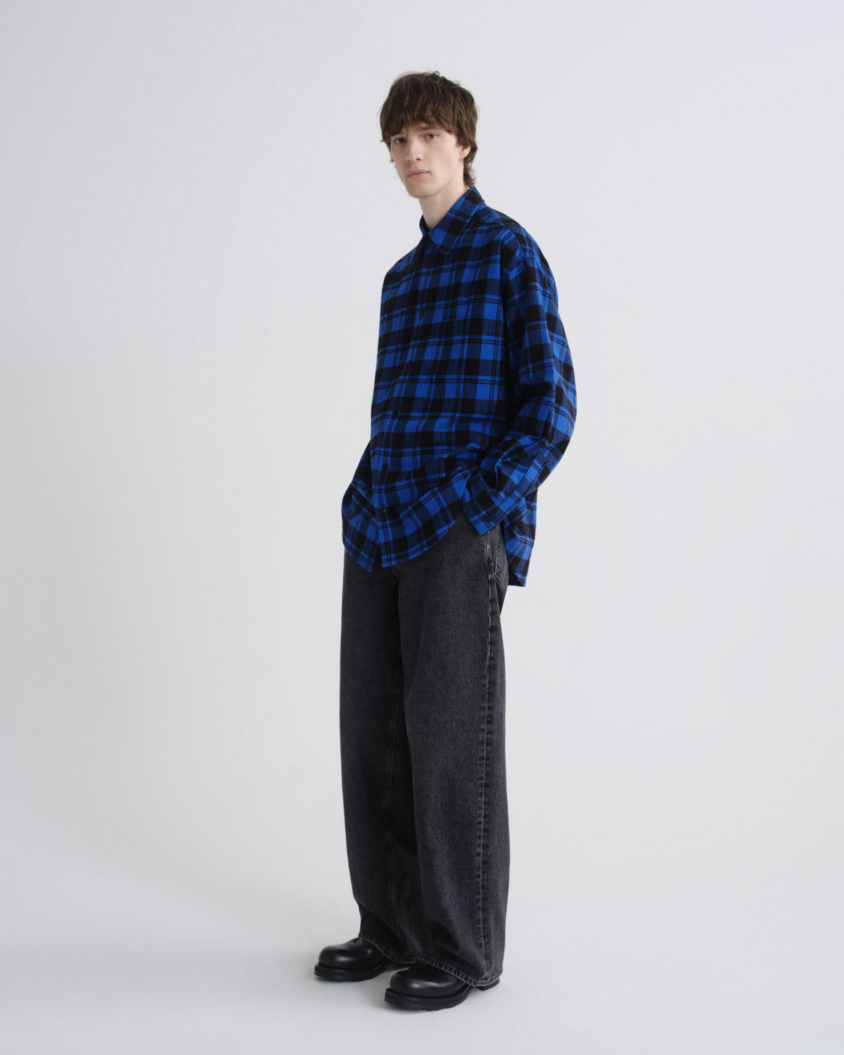 Person wearing a blue and black checkered shirt with dark pants on a white background