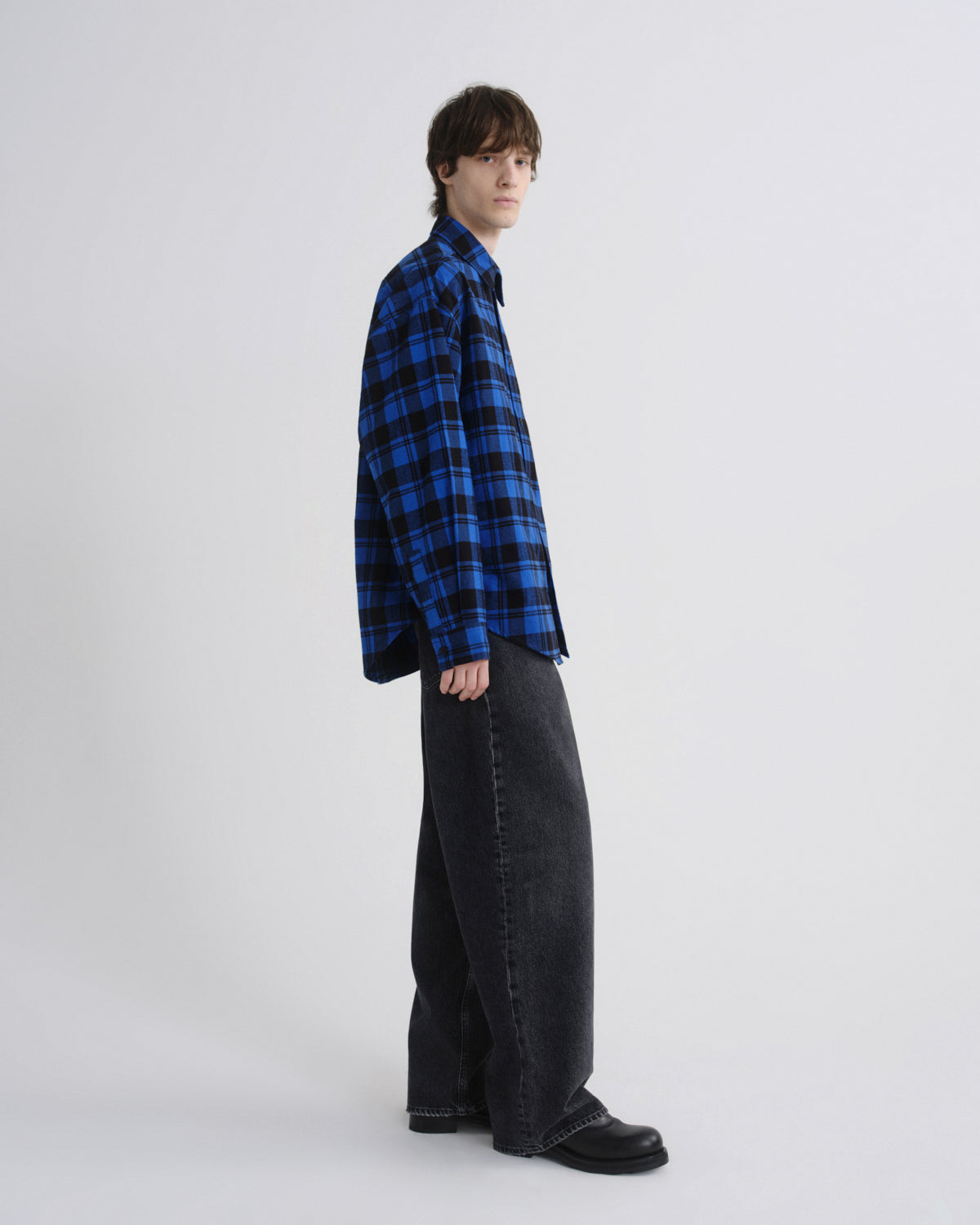 Person wearing a blue plaid shirt and black pants on a white background