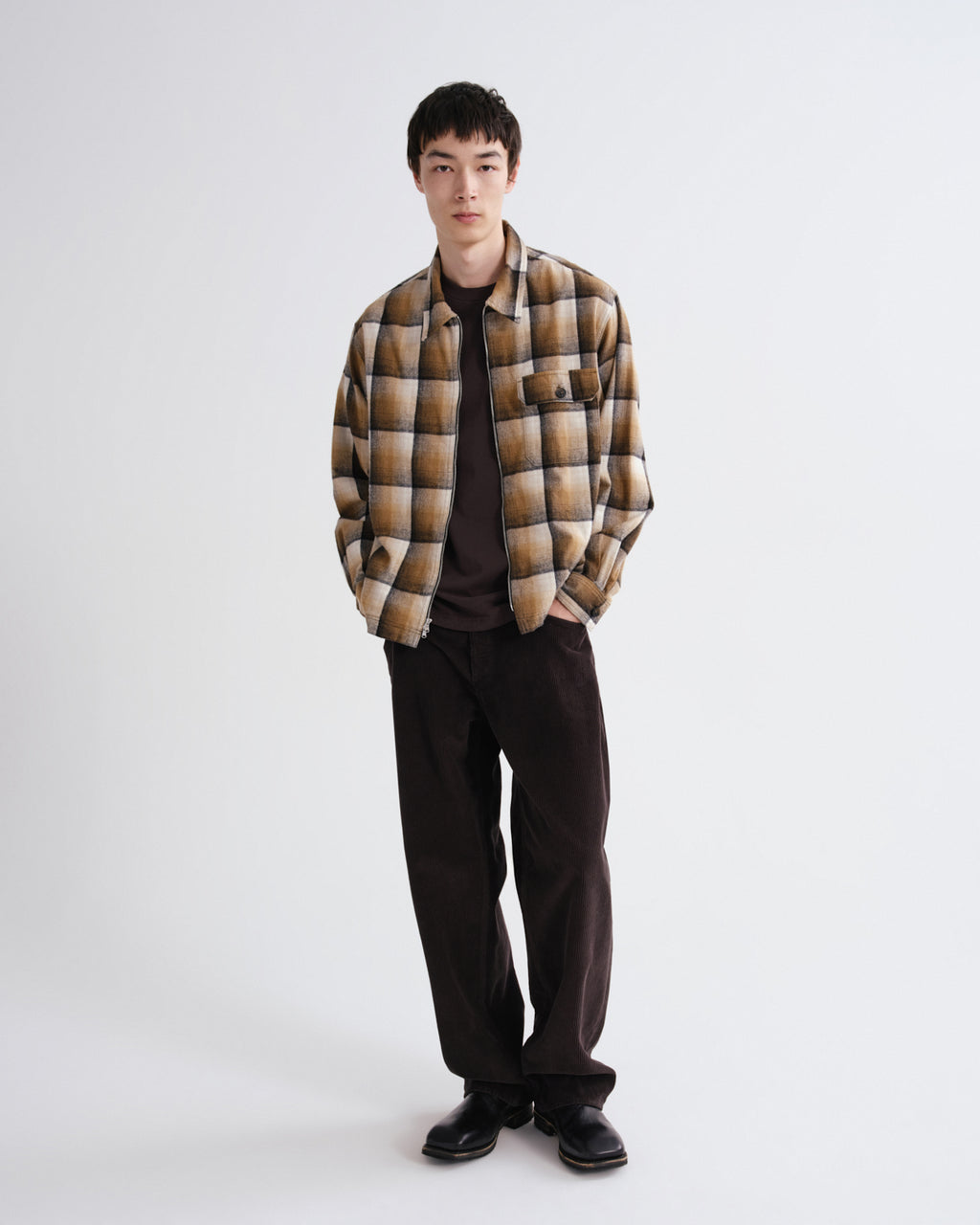 Person wearing a plaid shirt over a dark sweater with black pants on a white background