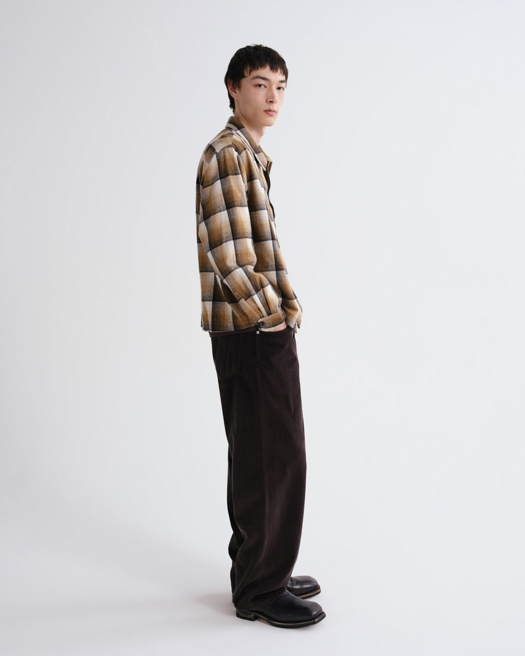 Person wearing a plaid shirt and dark pants on a white background