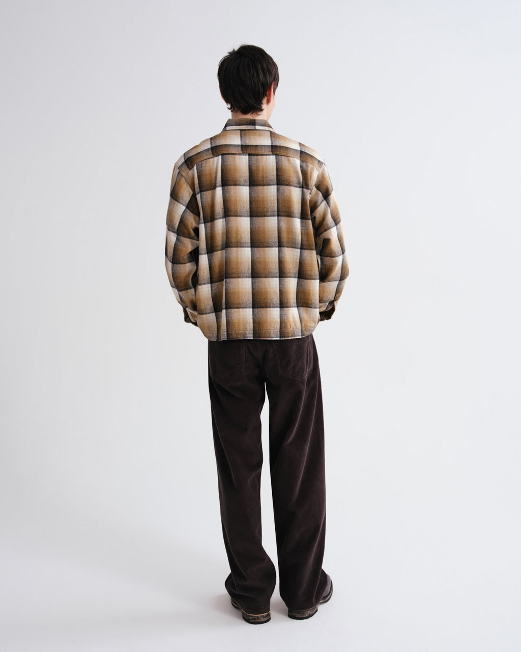 Person wearing a plaid shirt and dark pants on a white background