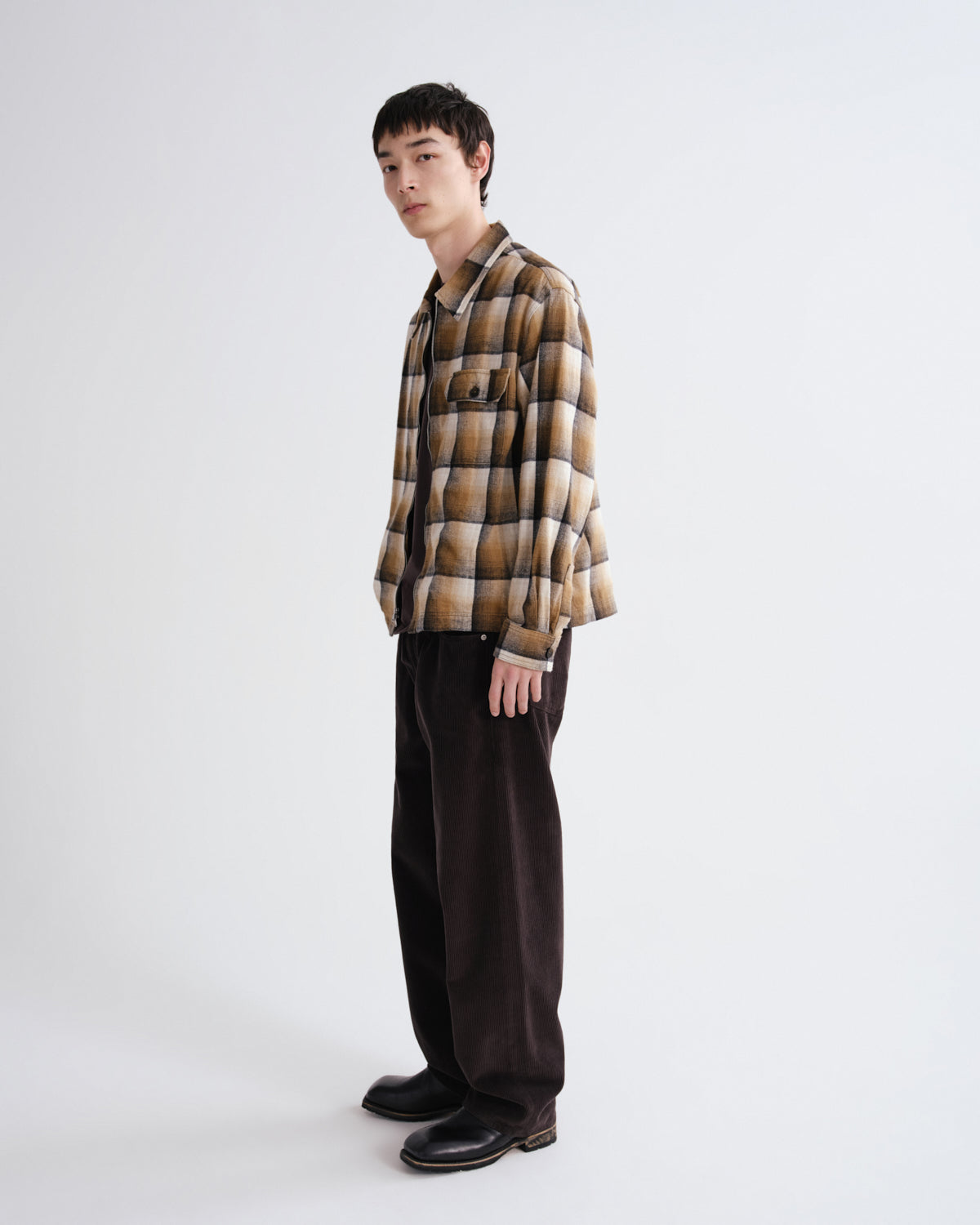 Person wearing a plaid shirt and dark pants on a white background