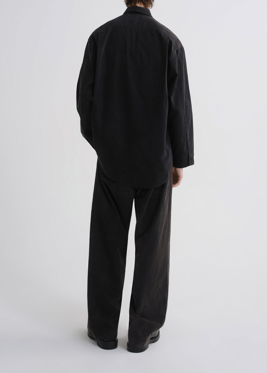 A person shown from the back wearing a loose black long-sleeve shirt and matching black wide-leg pants against a grey background.
