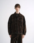 Person wearing a dark brown denim jacket with matching dark brown pants and black shoes on a grey background