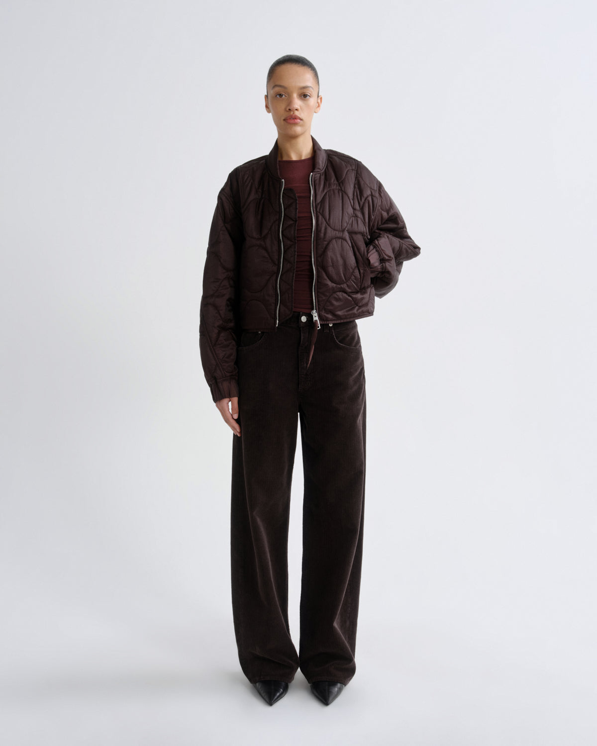 Person wearing a dark brown jacket and pants on a white background