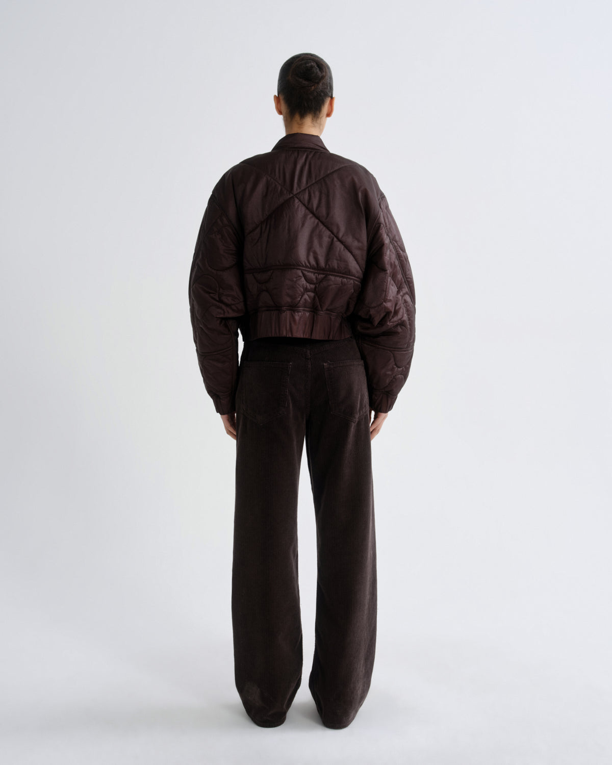 Person wearing a brown quilted jacket and pants on a white background
