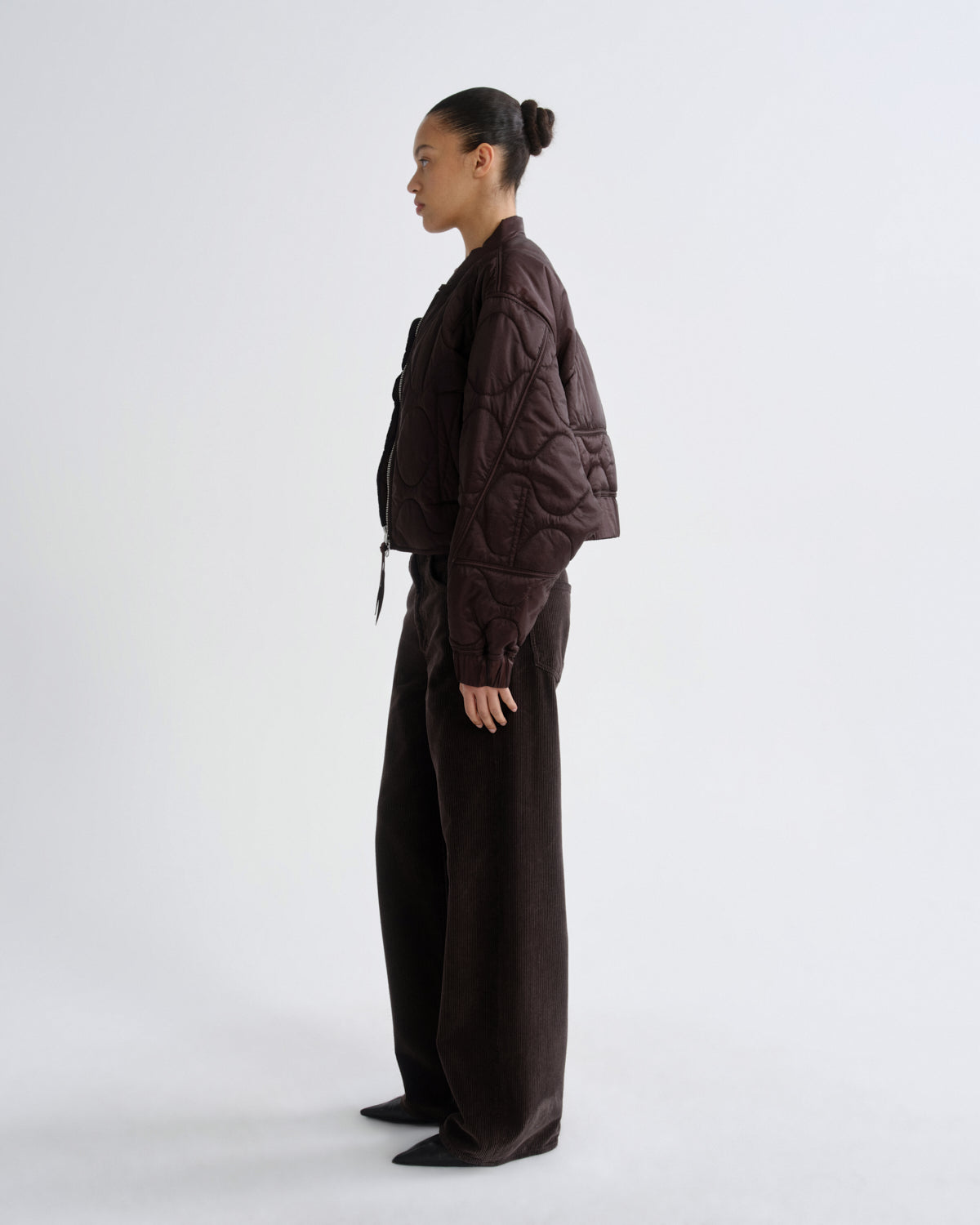 Person wearing a brown quilted jacket and pants on a white background