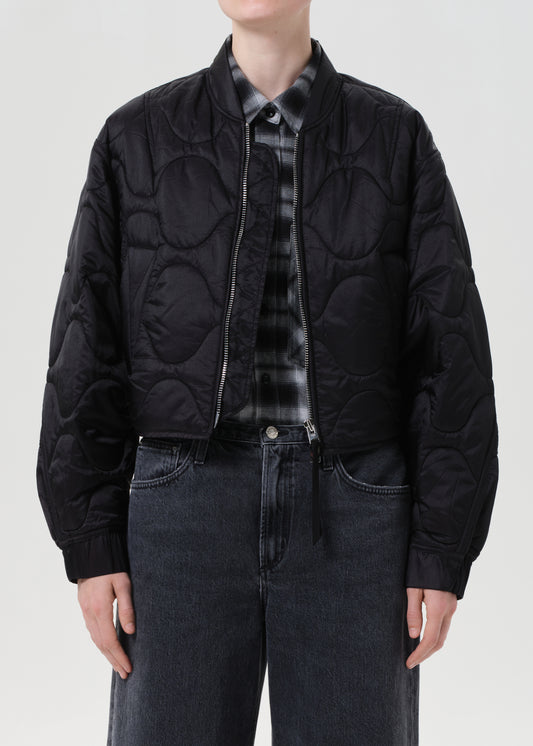 Person wearing a black quilted jacket over a patterned shirt on a white background
