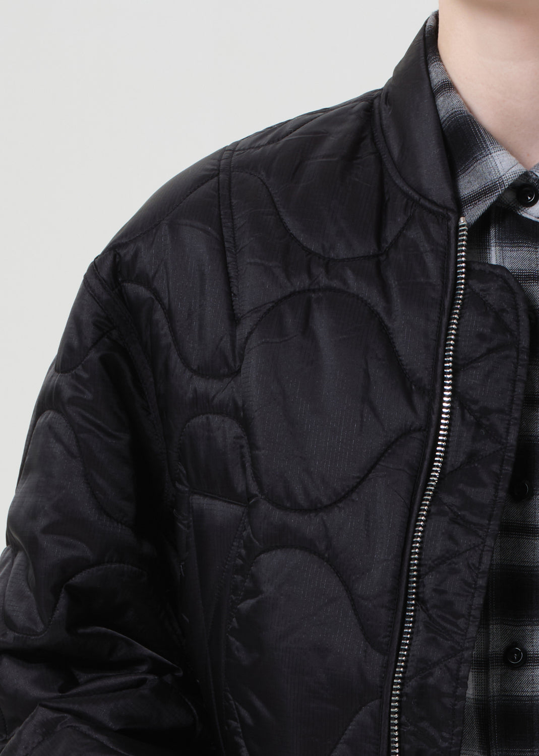 Black quilted jacket worn over a plaid shirt on a plain background