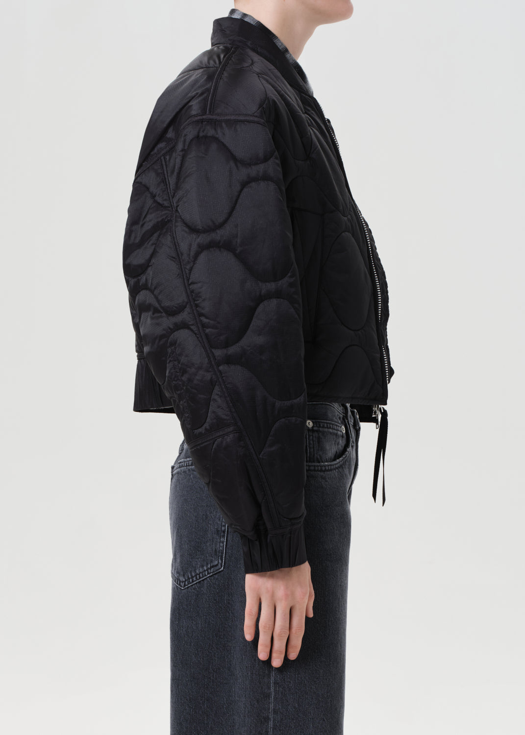 Person wearing a black quilted jacket and dark jeans on a light gray background