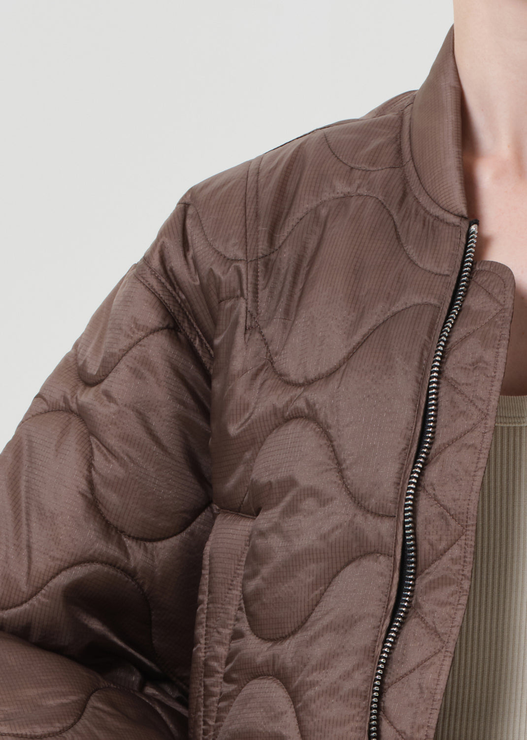 Close-up of a brown quilted jacket with a zipper on a light gray background