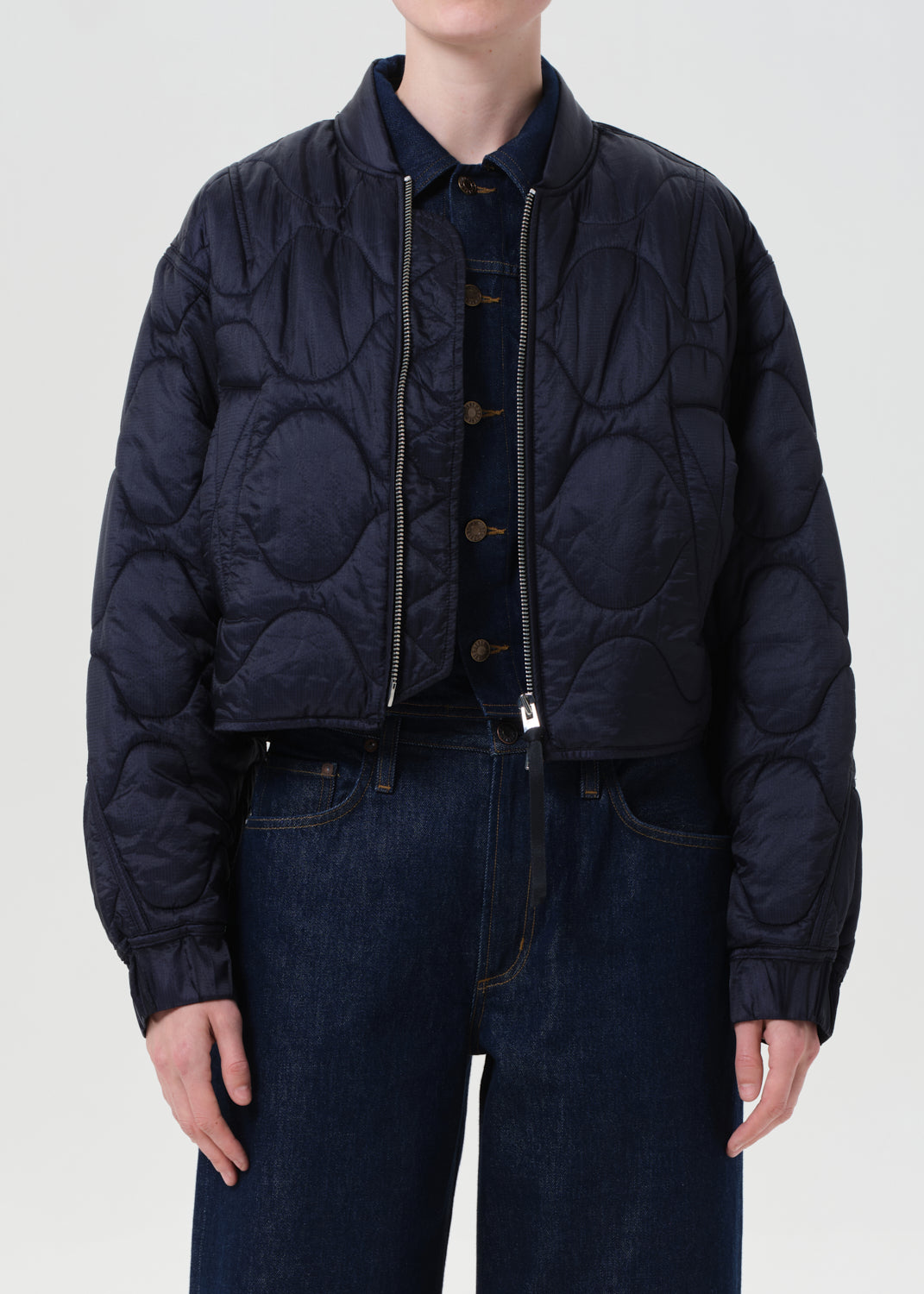 Person wearing a dark quilted jacket and jeans on a white background