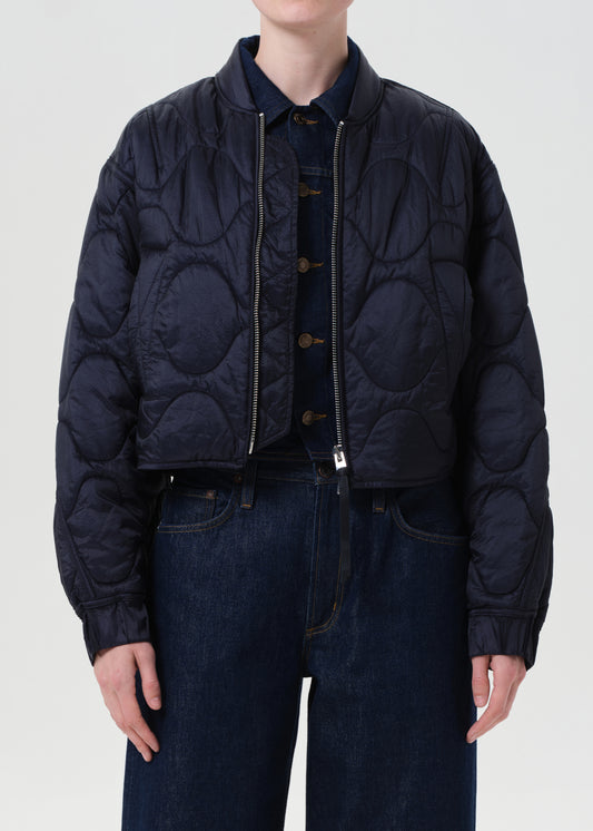 Person wearing a dark quilted jacket and jeans on a white background