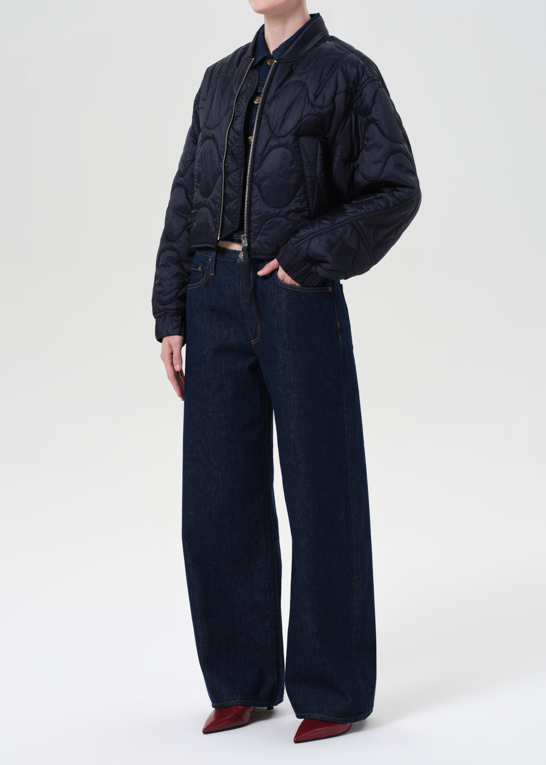 Person wearing a dark quilted jacket and wide-leg jeans on a white background