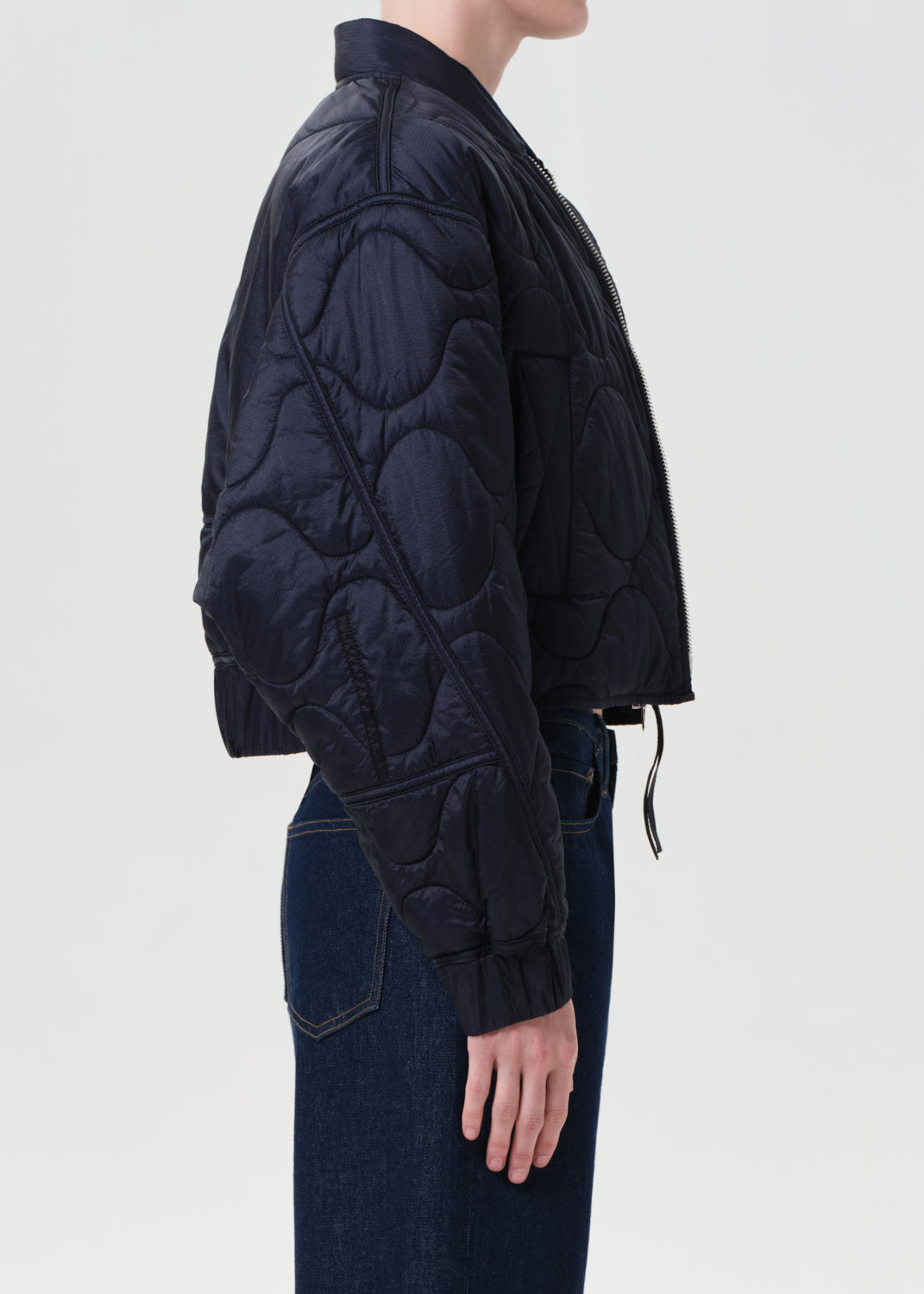 Person wearing a dark quilted jacket on a light gray background