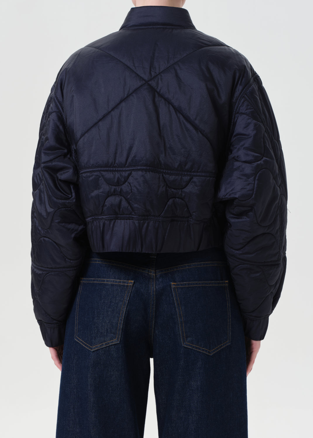 Person wearing a dark blue quilted jacket and jeans on a white background