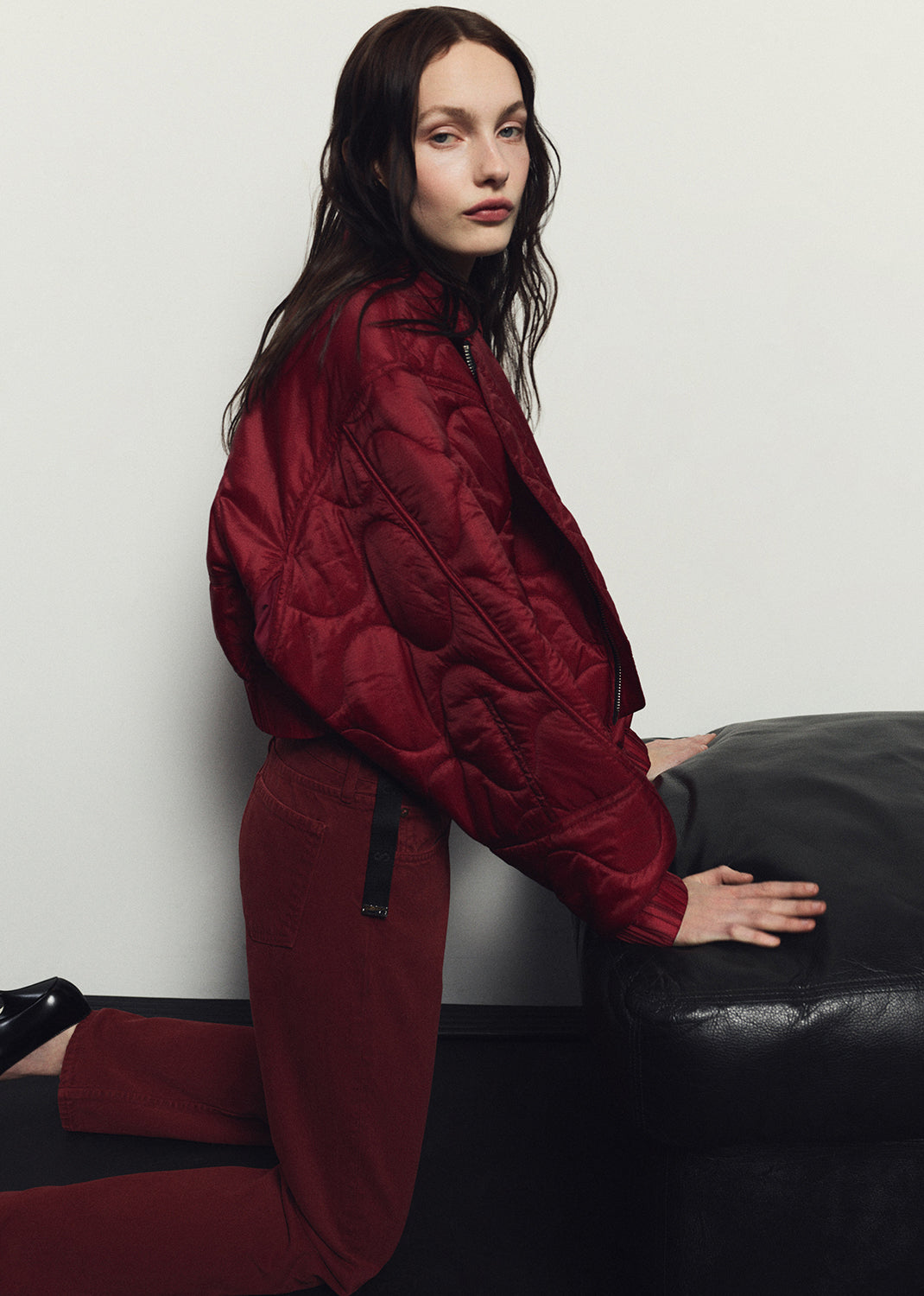 Person wearing a red outfit sitting on a black surface against a white wall