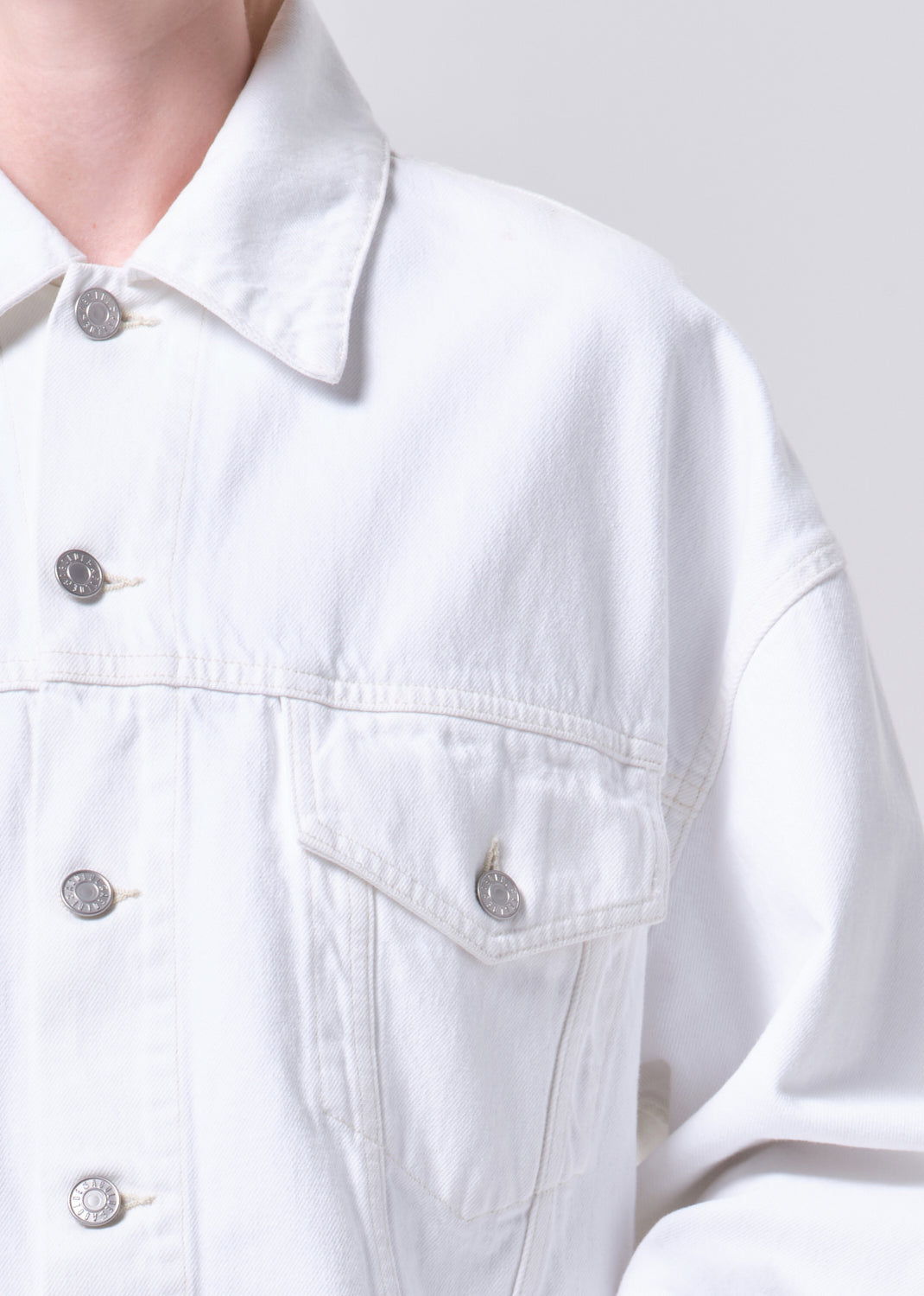 Close-up of a white denim jacket with button details on a plain background