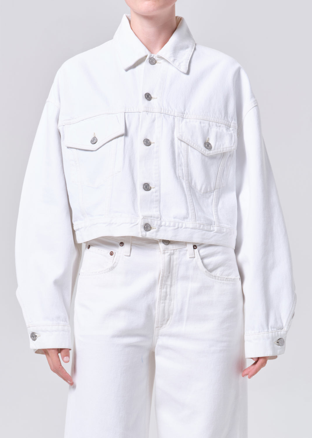 Person wearing a white denim jacket and pants on a plain background