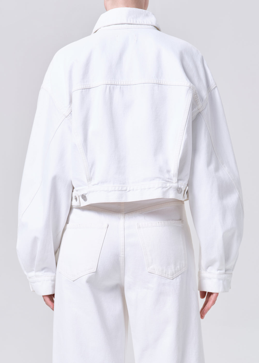 Person wearing a white denim jacket and pants on a plain background