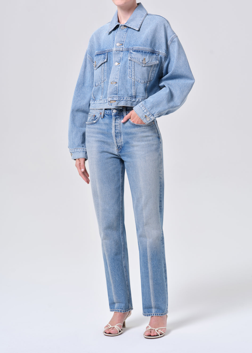 Person wearing a light blue denim jacket and jeans on a white background