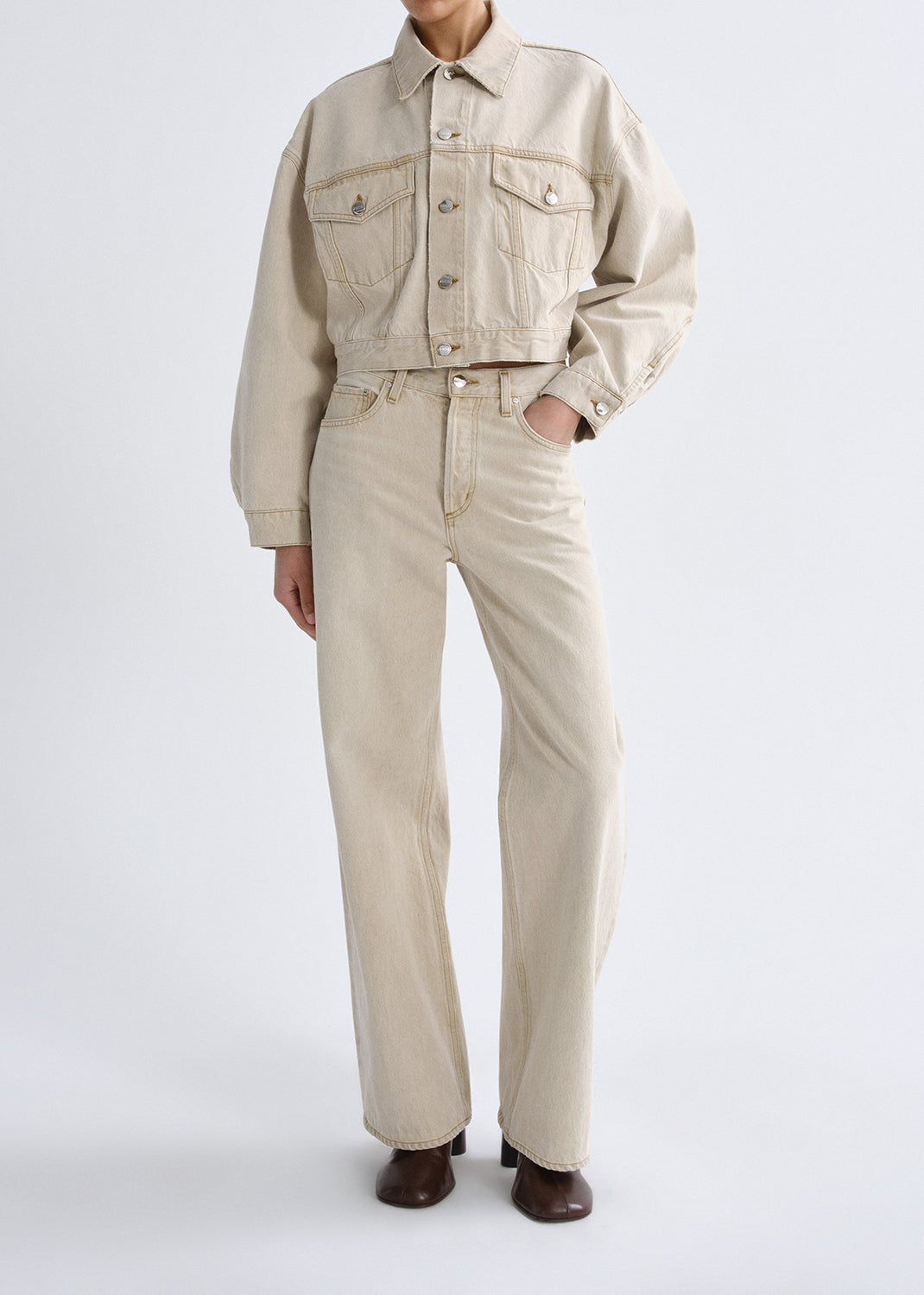 Person wearing a beige denim jacket and pants on a grey background