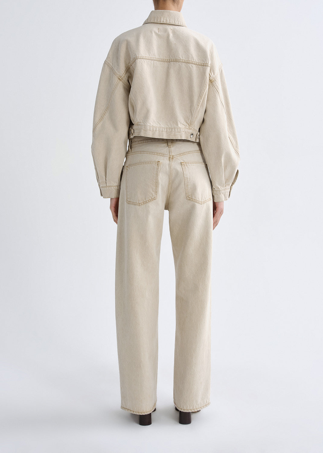 Person wearing a beige jacket and pants on a grey background