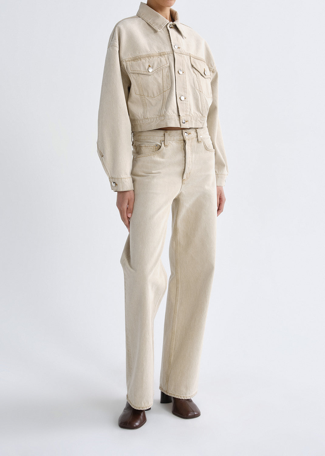 Person wearing a beige jacket and pants set on a grey background
