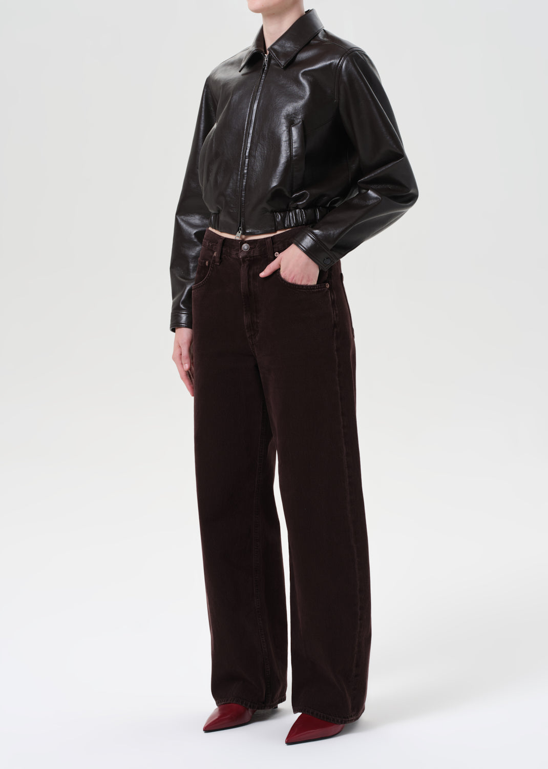 Person wearing a shiny black shirt and dark brown pants on a white background