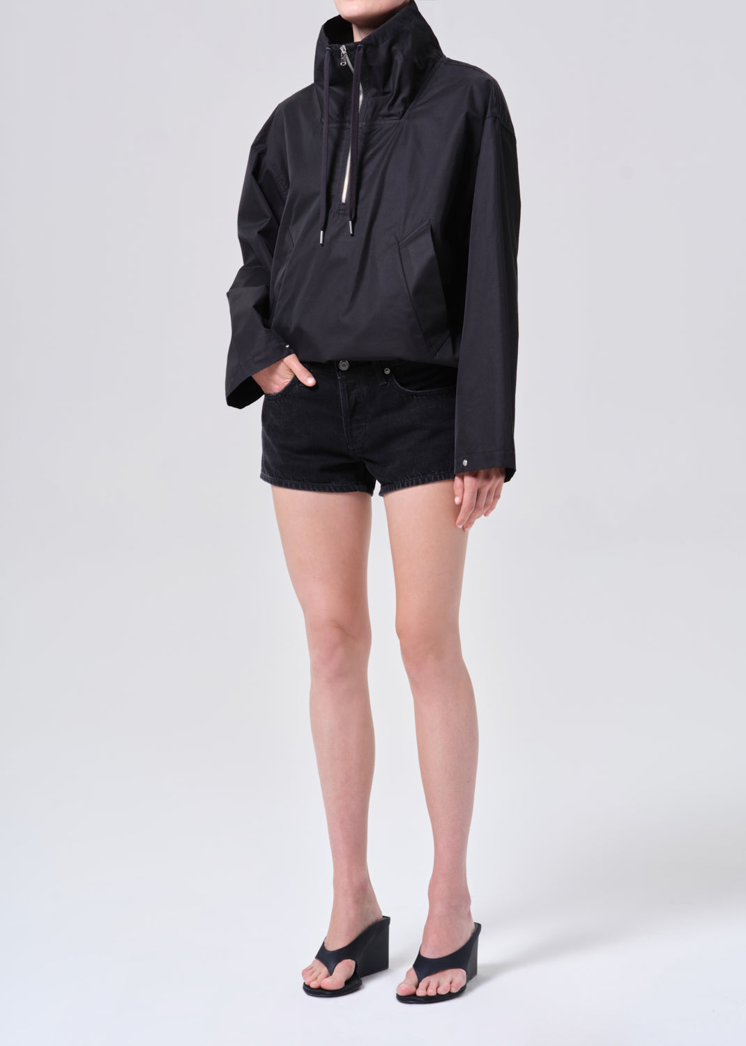 Person wearing a black jacket and shorts on a white background