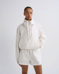 A model wearing a matching off-white cropped windbreaker jacket and shorts set, photographed against a seamless light gray studio background.