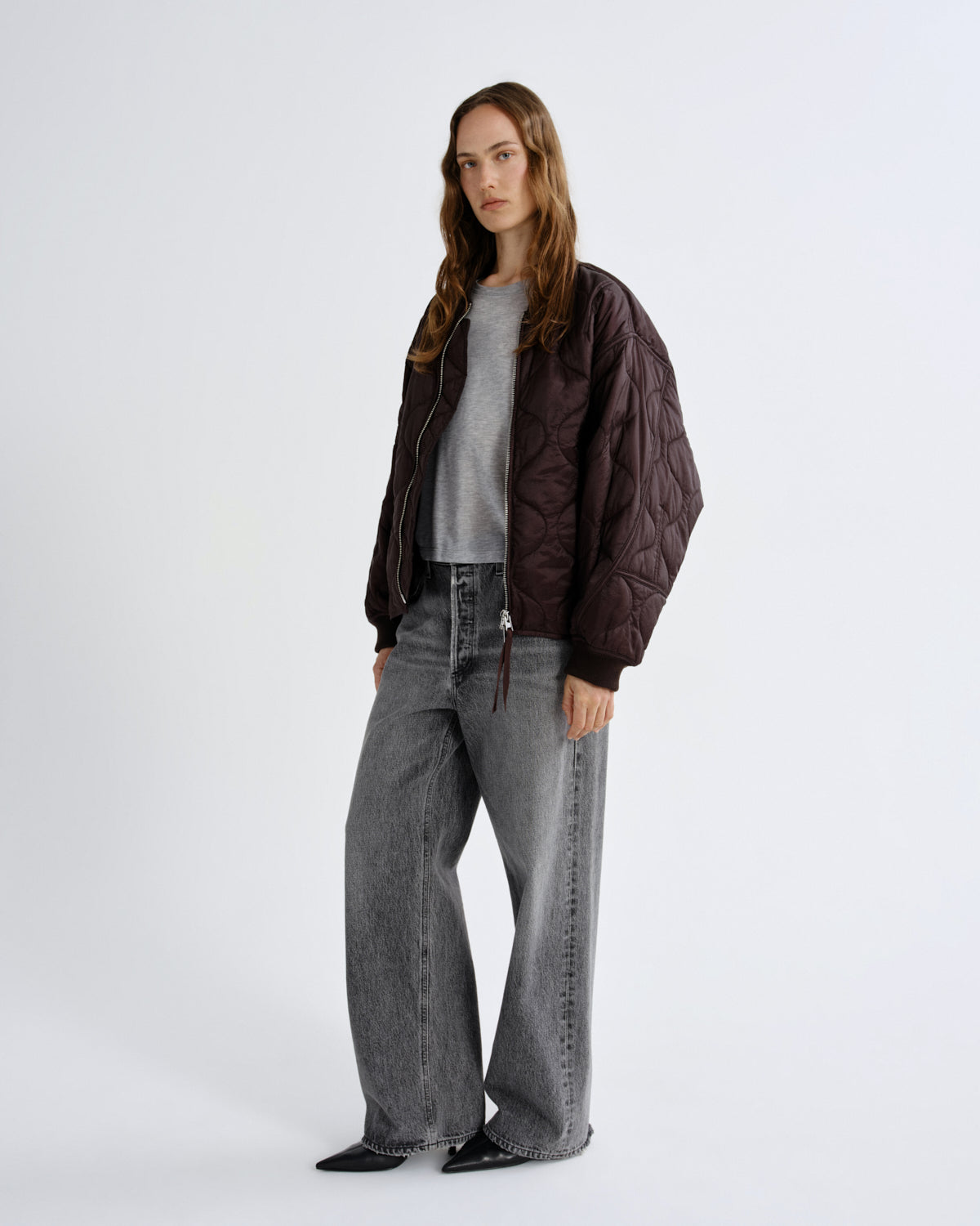 Person wearing a brown jacket and gray jeans on a white background