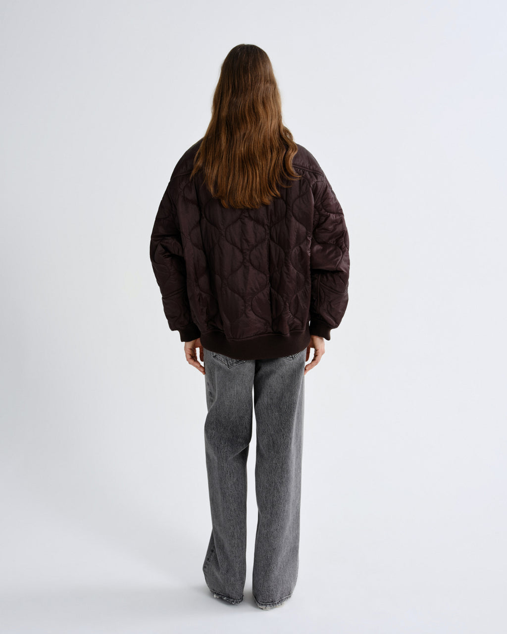 Person wearing a brown quilted jacket and gray pants on a white background