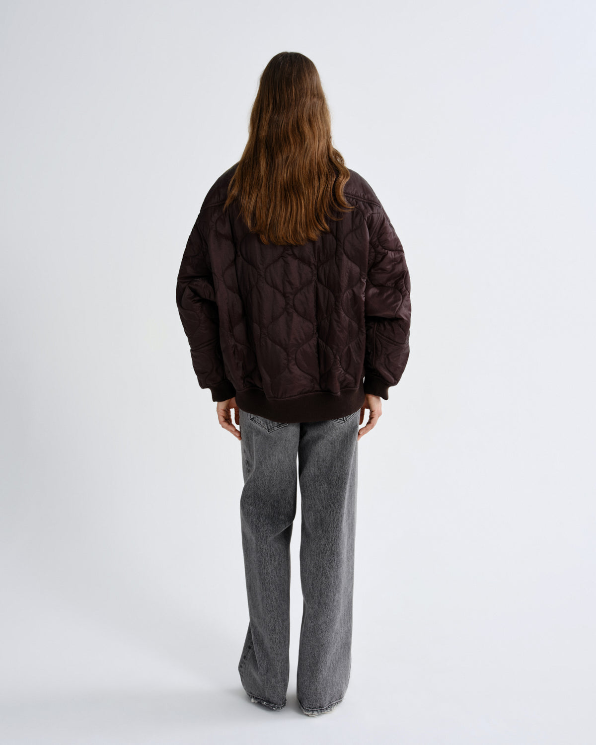 Person wearing a brown quilted jacket and gray pants on a white background