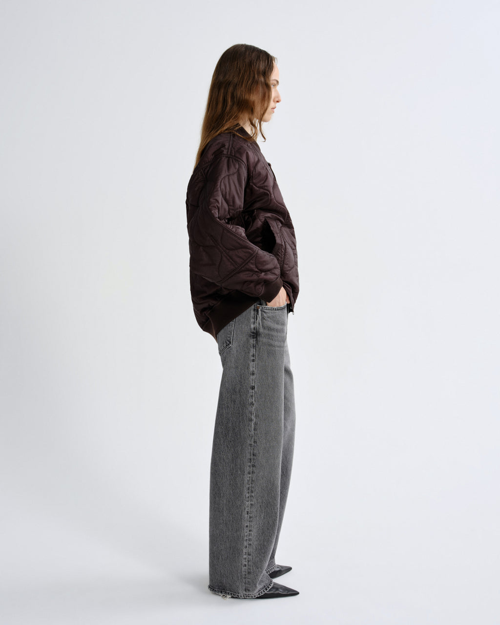 Person wearing a dark jacket and gray jeans standing against a white background