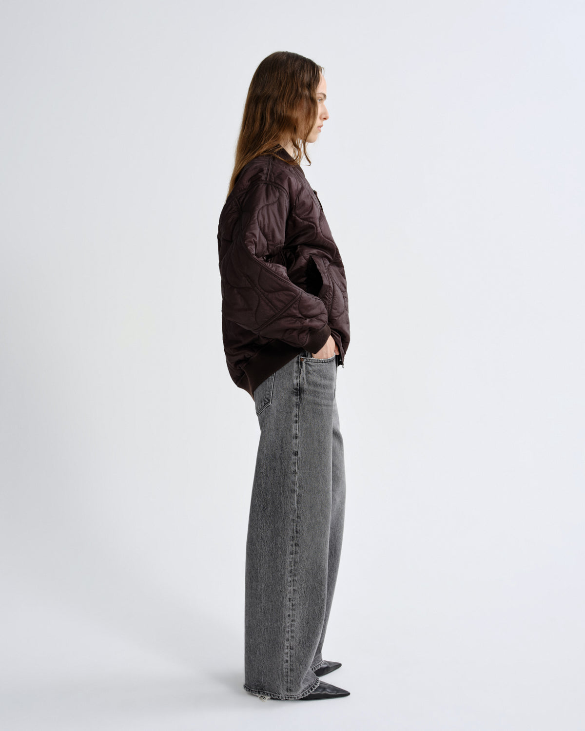 Person wearing a dark jacket and gray jeans standing against a white background