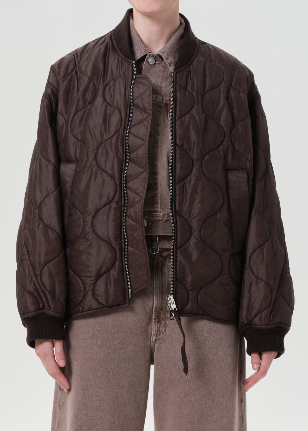 Person wearing a brown quilted jacket on a white background