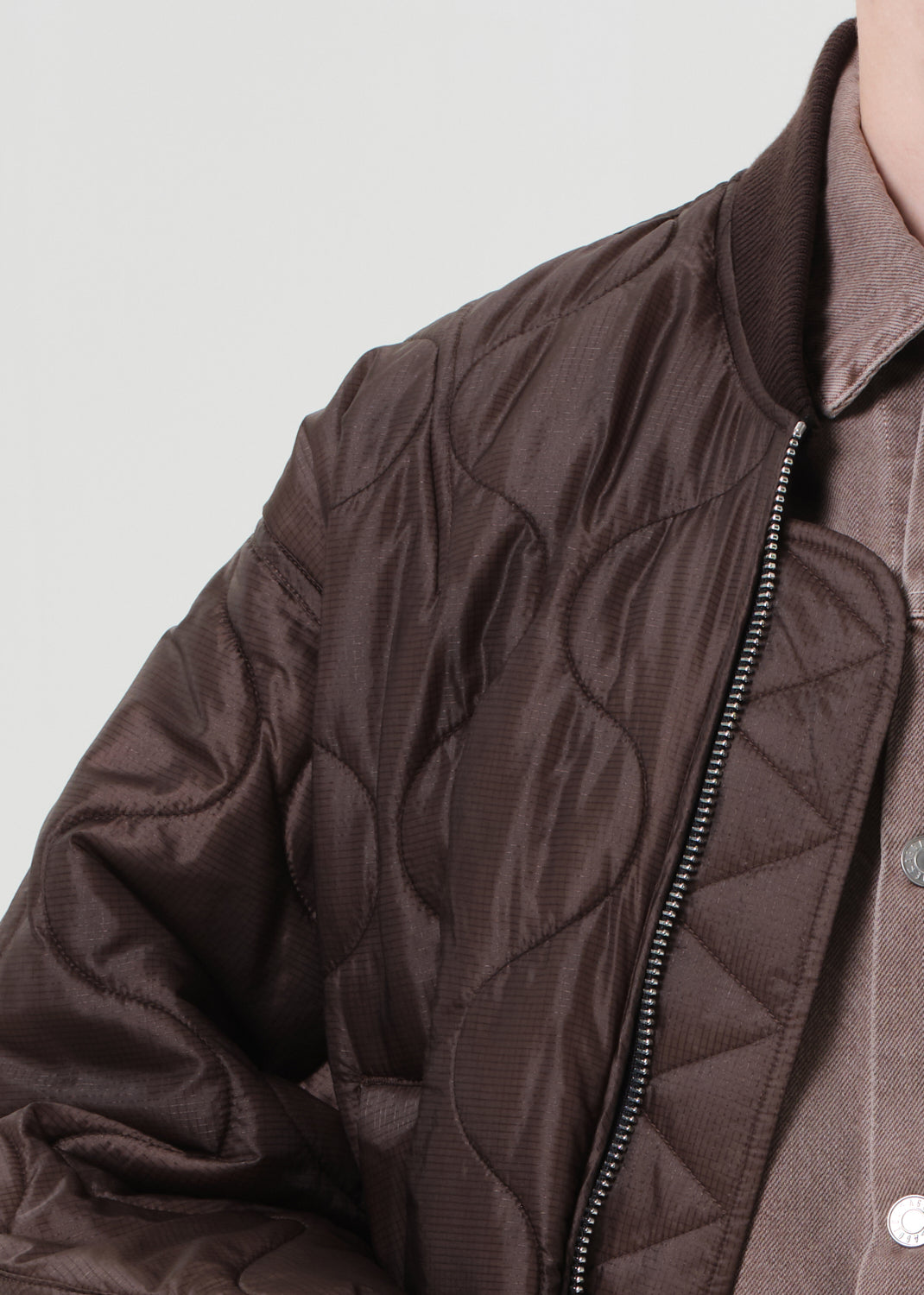 Brown quilted jacket with a zipper on a light gray background