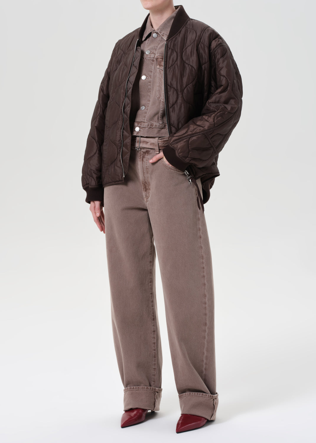 Person wearing a brown quilted jacket over a shirt with beige pants on a white background
