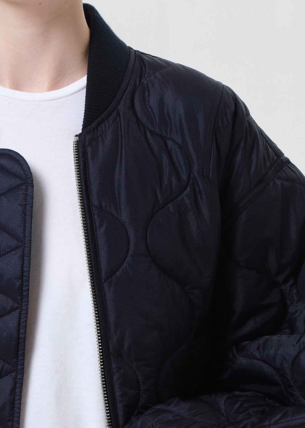 Person wearing a dark blue quilted jacket over a white shirt on a plain background